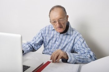 Senior businessman using laptop while reading file at office desk