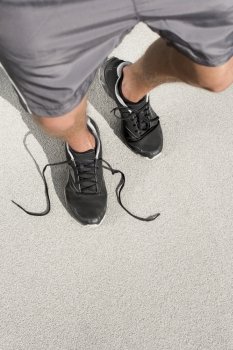 Low section of sporty man with untied shoelace standing on street