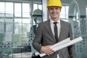 Portrait of smiling young architect holding rolled up blueprints in industry