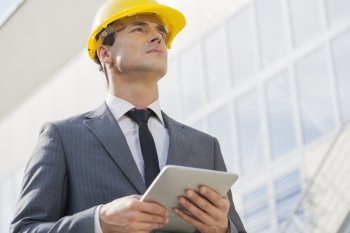 Young male architect holding tablet PC against building