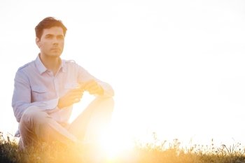 Thoughtful man looking away while sitting on grass against clear sky