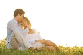 Romantic young couple sitting on grass against clear sky