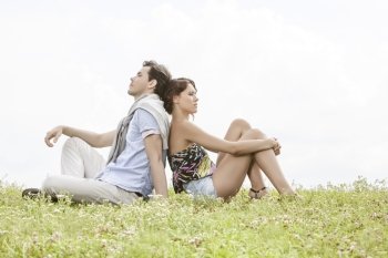 Full length of thoughtful young couple sitting back to back in park