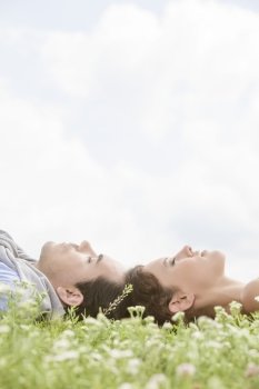 Side view of young couple sleeping on grass against sky