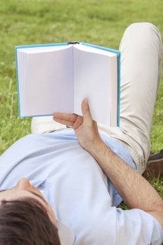 Young man holding book while lying in park