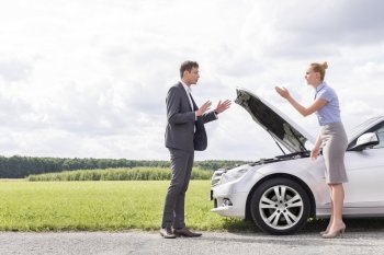Full length side view of business couple arguing over broken car at countryside