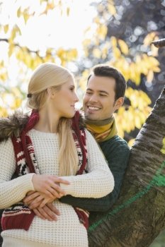 Happy young man hugging woman while leaning on tree trunk during autumn in park