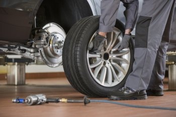 Low section of male mechanic repairing car’s tire in repair shop