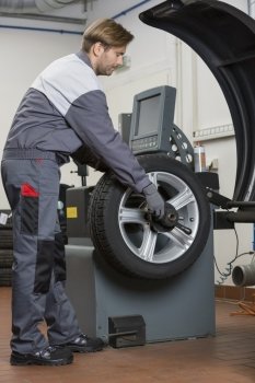 Side view of male mechanic repairing car’s wheel in workshop