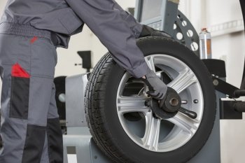 Midsection of male mechanic repairing car’s wheel in repair shop