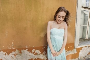 Shy teenage girl in tube dress standing against wall