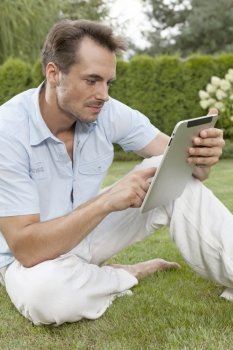 Young man using digital tablet while sitting on grass in park
