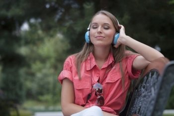 Relaxed young woman listening to headphones on park bench