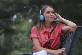 Beautiful young woman listening musing through headphones in park
