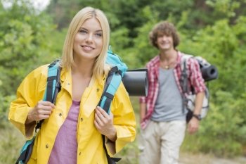 Smiling female backpacker looking away with man standing in background at forest