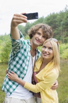 Happy young couple taking self portrait through cell phone in field