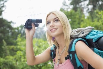 Young female hiker using binoculars in forest