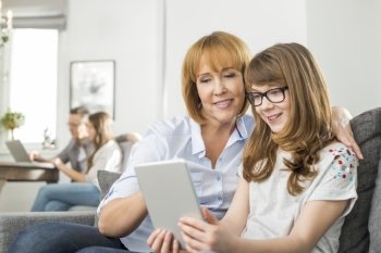 Loving mother and daughter using tablet PC with family sitting in background at home