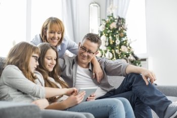 Family using tablet PC on sofa with Christmas tree in background