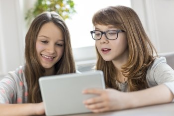 Sisters using digital tablet at table in house