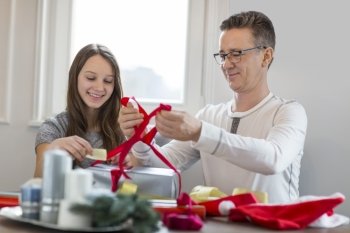 Smiling father and daughter wrapping Christmas present at home