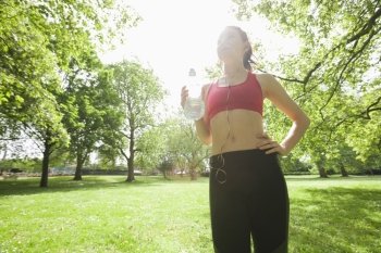 Low angle view of fit woman listening to music while holding water bottle in park