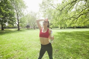 Tired fit woman with water bottle listening to music in park