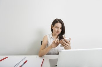 Young businesswoman text messaging through cell phone at desk in office