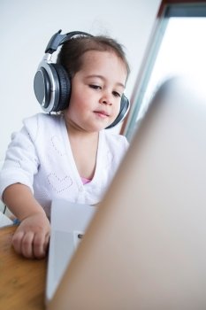 Little girl wearing headphones while looking at laptop at table in house