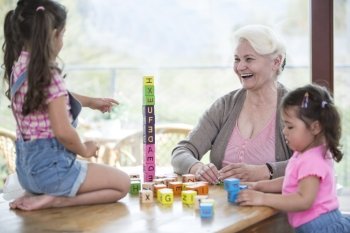 Happy grandmother and granddaughters playing with alphabet blocks at table