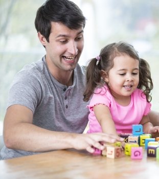 Happy father and daughter playing with building blocks at table in house