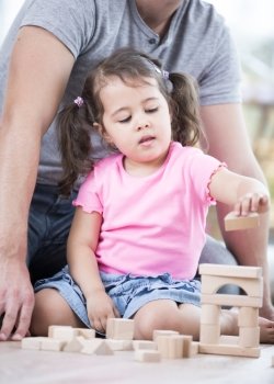 Little girl playing with wooden blocks against father in house
