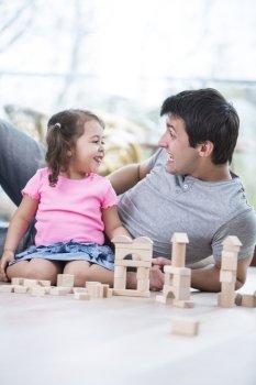 Cute girl teasing father while playing with wooden building blocks at home