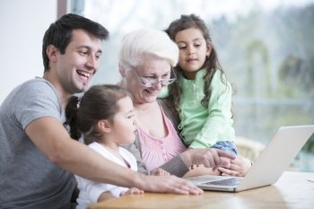 Happy three generation family using laptop at table in house