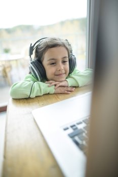 Cute little girl listening to music on headphones while using laptop at home