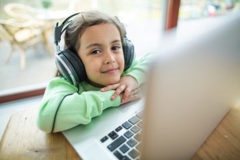 Portrait of cute girl listening to music on headphones with laptop at table