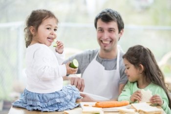 Happy father preparing sandwiches while daughters eating at home