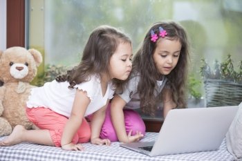 Cute little sisters using laptop on bed at home