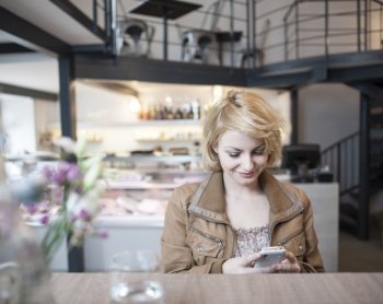 Happy young woman reading text message on cell phone in cafe