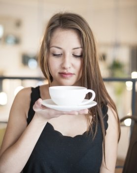 Beautiful young woman holding coffee cup and saucer at cafe