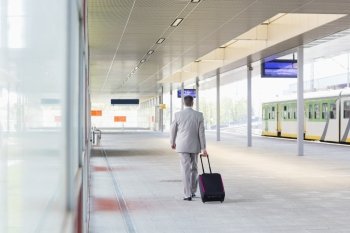 Full length rear view of businessman with luggage walking in railroad platform