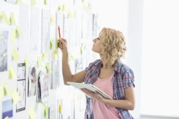 Creative businesswoman analyzing papers stuck on wall in office