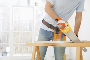 Midsection of man sawing wood in new house
