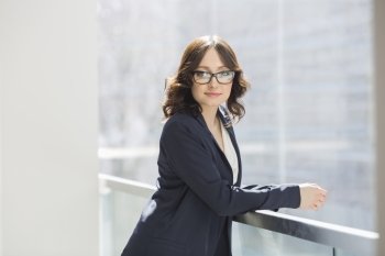 Portrait of confident young businesswoman leaning on railing in office