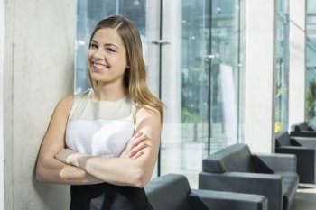 Portrait of happy businesswoman standing arms crossed at office lobby