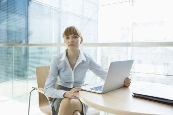 Portrait of beautiful businesswoman with laptop sitting at table in office