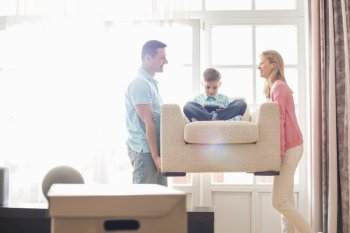 Happy parents carrying son on armchair in new house