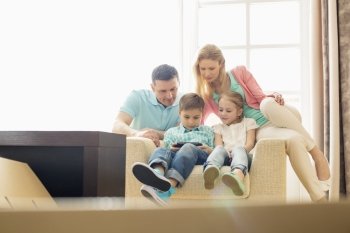 Family looking at boy playing hand-held video game at home