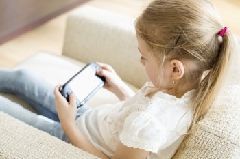 Rear view of girl playing hand-held video game at home