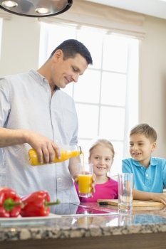 Father serving orange juice for children in kitchen